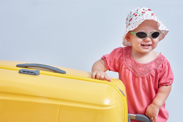 A cute little girl stands next to a large yellow suitcase. Travel with children. Space for text.