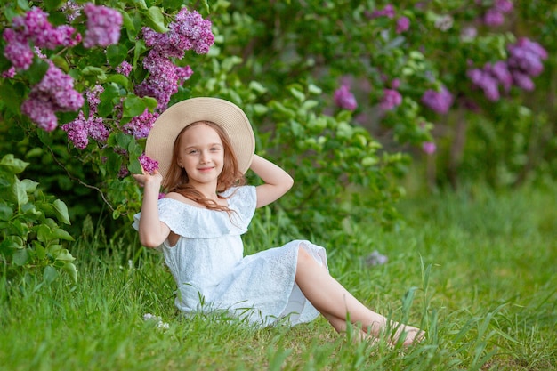 Cute little girl in a straw hat in spring in the lilac garden