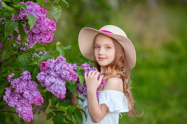 Cute little girl in a straw hat in spring in the lilac garden