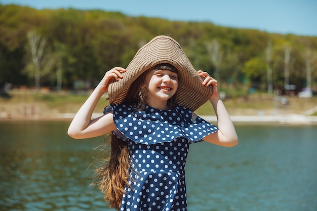 麦わら帽子をかぶったかわいい女の子が市の湖の近くの木の橋の上に立っています