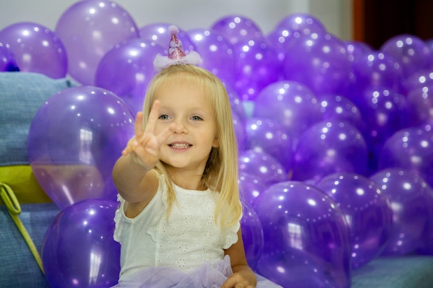 Cute little girl in stylish dress celebrating birthday day with purple balloons