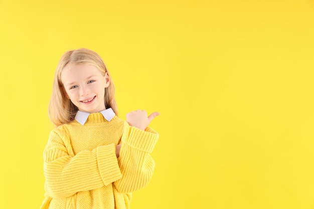 Cute little girl in sweater on yellow background