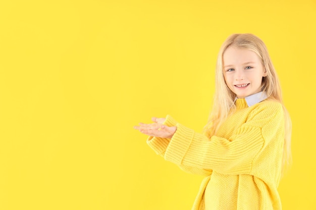 Cute little girl in sweater on yellow background