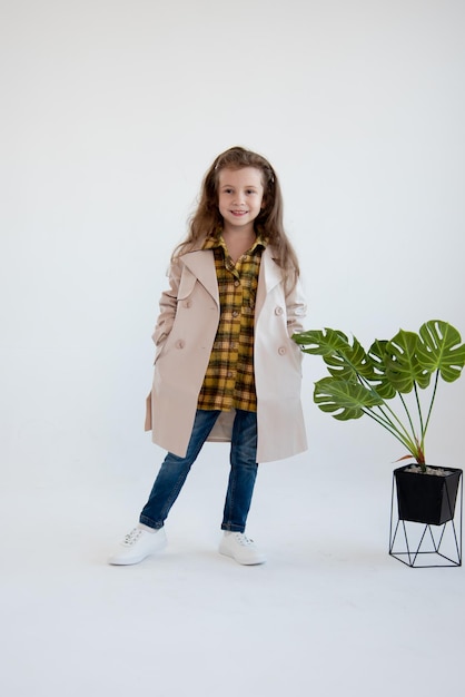 A cute little girl in trench coat stand on a white background Fashion Childhood