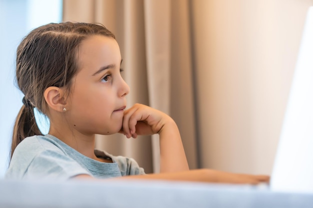 Bambina sveglia che utilizza il computer portatile a casa. istruzione, studio online, studio a casa, apprendimento a distanza, concetto di stile di vita dei bambini delle scolarette