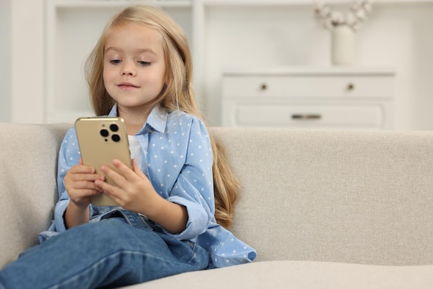家のソファでスマートフォンを使っているかわいい小さな女の子