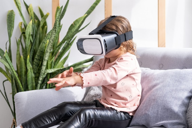 Cute little girl in virtual reality glasses at home happy kid using vr headset