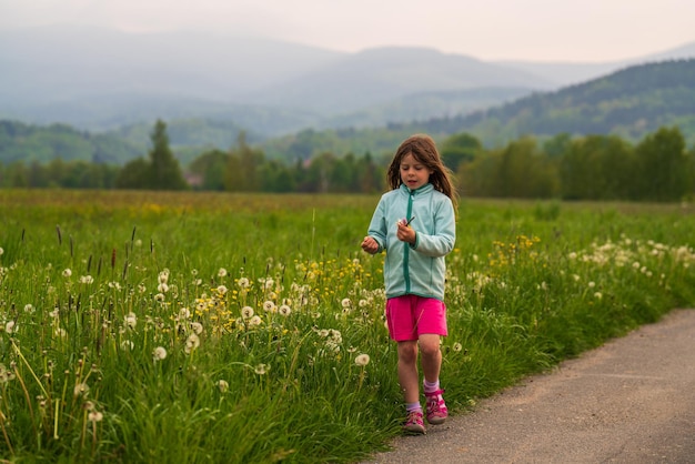 A cute little girl walks along a country road picking wildflowers and dandelions in a flower meadow