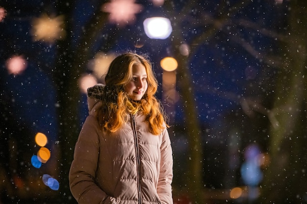 写真 かわいい女の子は、降雪の間に夜のお祭りの街を歩きます