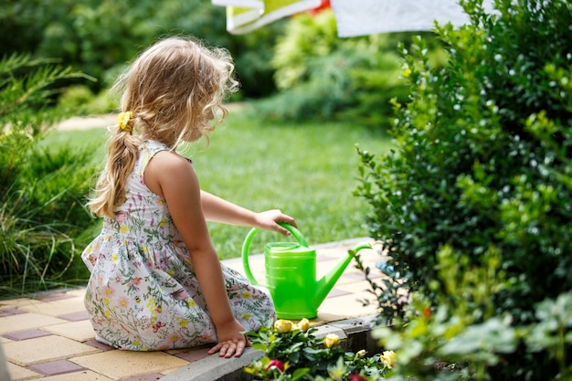 Милая маленькая девочка поливает растения в саду.
