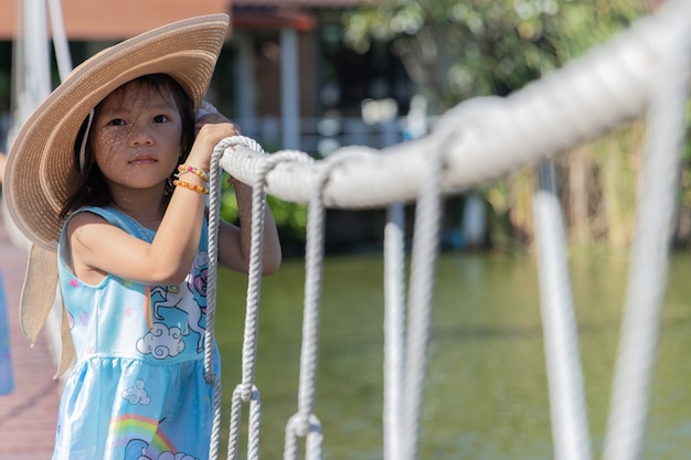 La bambina sveglia indossa un grande cappello e tiene il ponte di corda