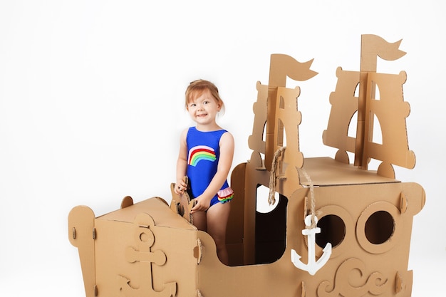 Cute Little girl wearing bright swimsuit playing with cardboard ship