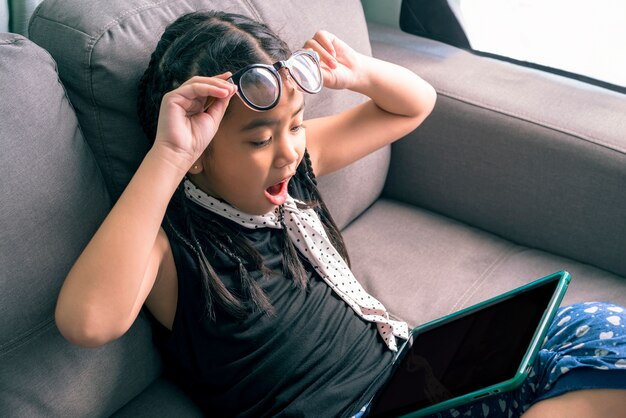 Cute little girl, wearing glasses, dreadlocks hair style, playing with computer at home 