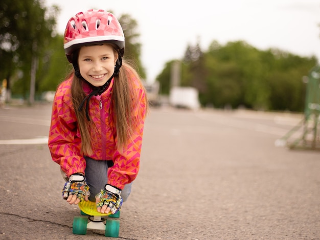 Cute little girl wearing helmet riding on a skateboard in beautiful summer park