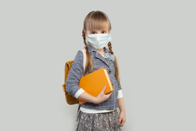 Cute little girl wearing medical protective face mask on white background