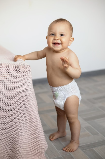 A cute little girl in a white diaper stands and learns to walk Lifestyle