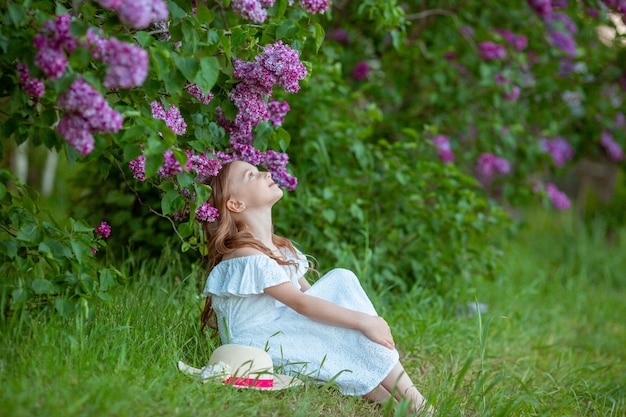 милая маленькая девочка в белом платье в цветущем сиреневом весеннем саду