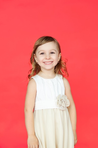 Милая маленькая девочка в белом платье улыбается в камеру