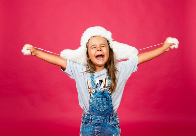 Cute little girl in a white fur hat against a pink wall. Fashion concept.