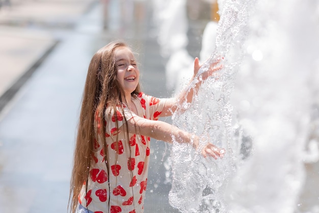 Cute little girl in white shirt with hearts playing with water in park