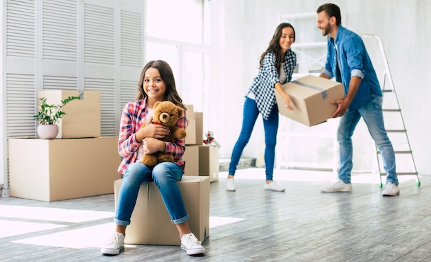 A cute little girl who is holding tightly her lovely teddy bear has a sincere wide smile on her face over being extremely happy about a new home