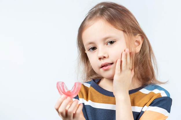 ブロンドの髪のかわいい女の子はピンクの歯科筋機能トレーナーを保持しています