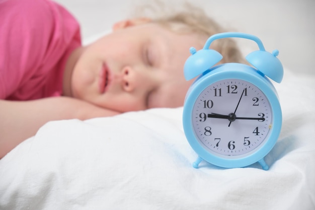 Cute little girl with blond hair and a pink tshirt sleeps on a white bed