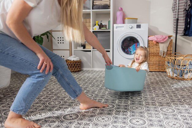 A cute little girl with blonde hair and blue eyes sits in a\
plastic blue clothes bowl