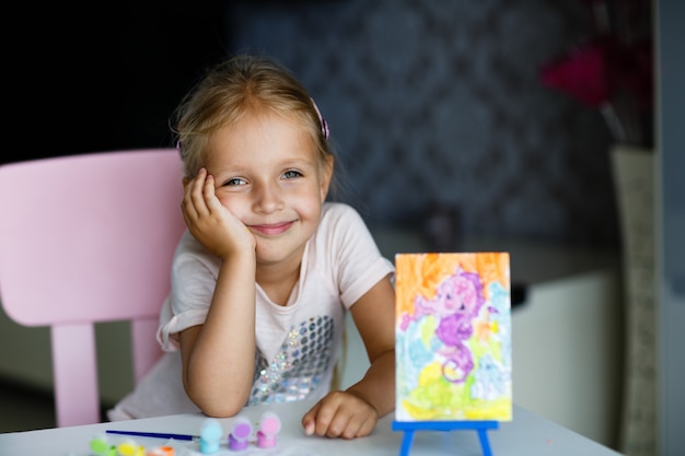 Cute Little Girl with blonde hair Painting Picture at home. 