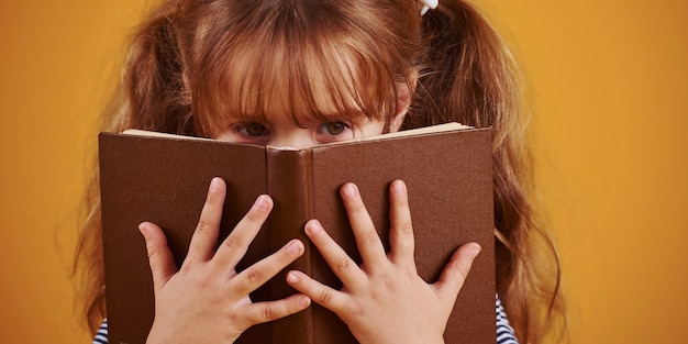 Фото Милая маленькая девочка с книгой в руках в студии желтом фоне.