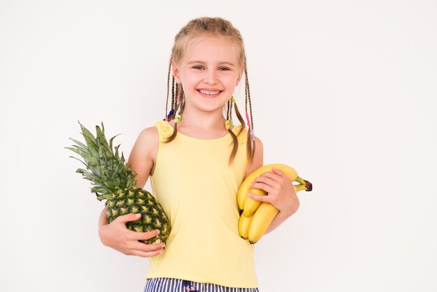 Cute little girl with braided hair holding bananas and pineapple