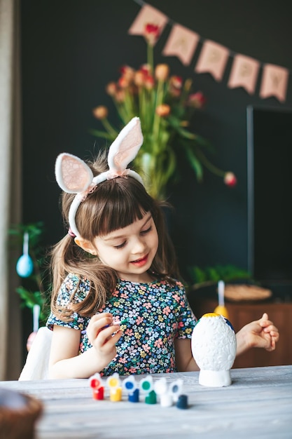 Cute little girl with bunny ears painting Easter egg