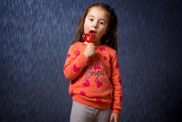 Foto bambina sveglia con caramelle a forma di cuore su sfondo blu