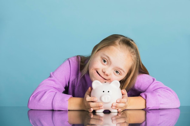 Photo cute little girl with down syndrome saving money in a piggy bank