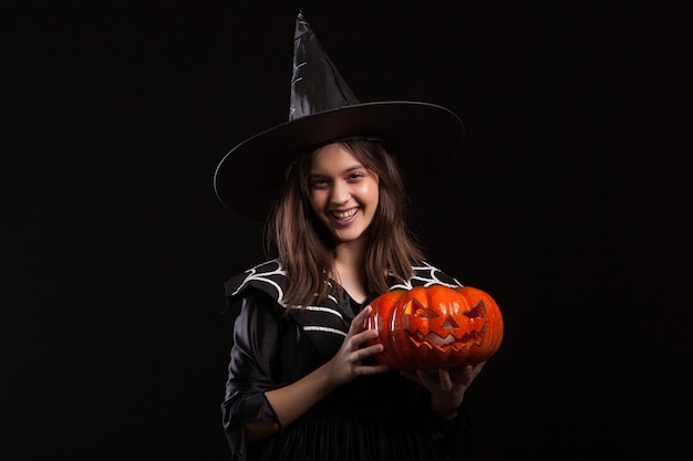 Cute little girl with a evil laugh doing sorcery with a pumpking for halloween. Adorable kid in a witch costume for halloween.