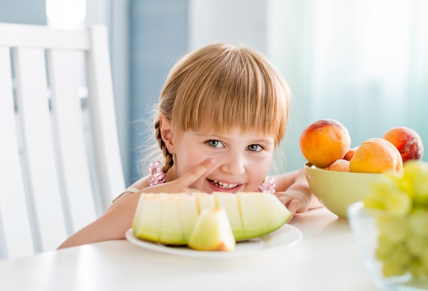 Bambina sveglia con i frutti sul tavolo