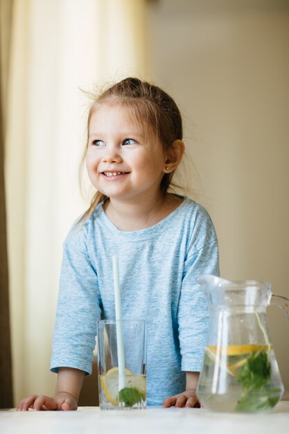 Photo cute little girl with glass of water in the kitchen