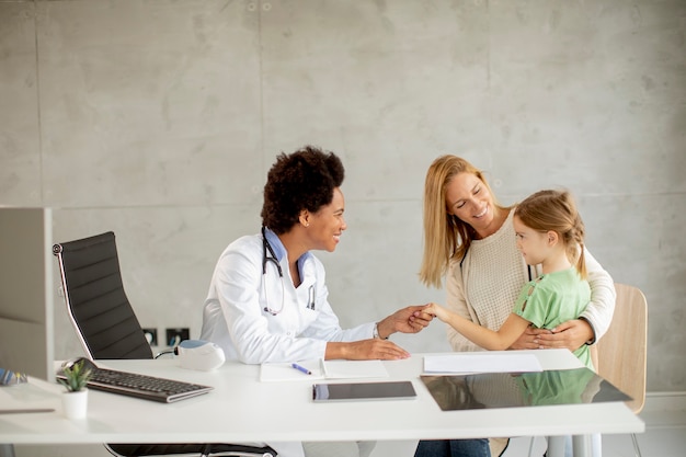 Cute little girl with her mother at the pediatrician examination by African american female doctor