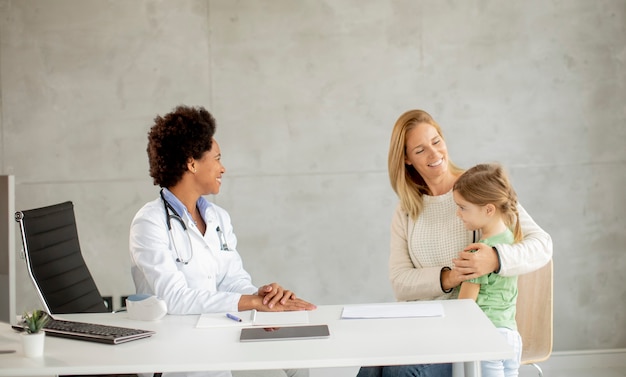 Cute little girl with her mother at the pediatrician examination by African american female doctor