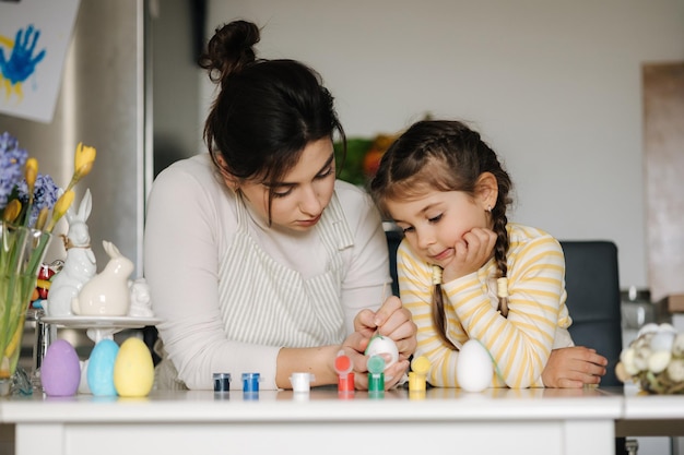 Cute little girl with her mother preparing for painting easter eggs mom and daughter look to each