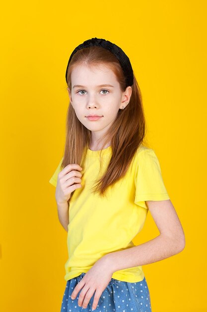 A cute little girl with long brown hair in a yellow Tshirt is standing in the studio on a yellow background Isolate Childhood games classes school hobbies