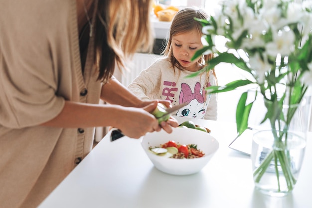 Cute little girl with long hair help to cook her mother in the kitchen at home Daughter and mom cooking food together