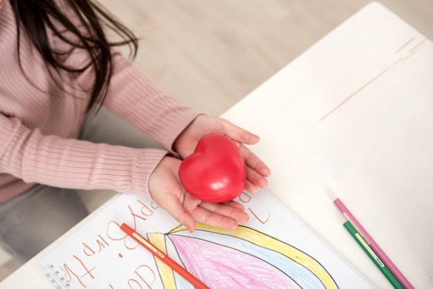 Foto bambina sveglia con capelli lunghi che giocano con un cuore rosso