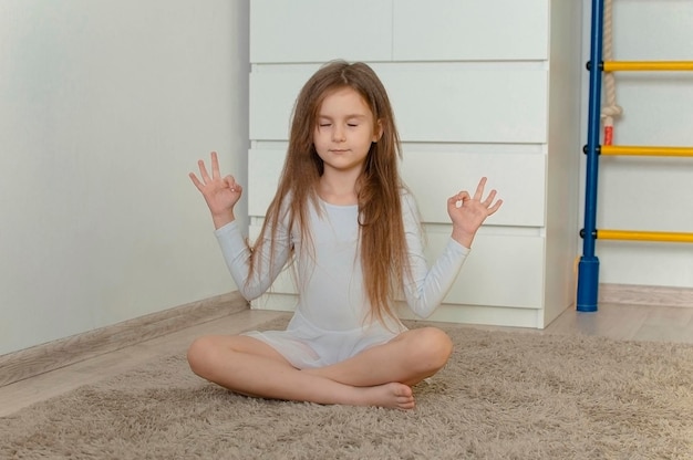 A cute little girl with long hair practices yoga pose in her room The concept of child development