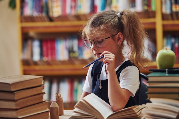 Милая маленькая девочка с косичками находится в библиотеке