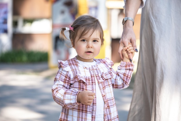 a cute little girl with ponytails in a plaid shirt is holding mother's hand