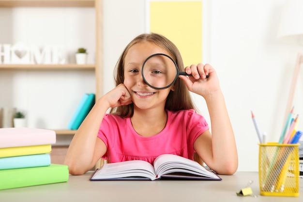 Cute little girl with poor eyesight reads with a magnifying glass