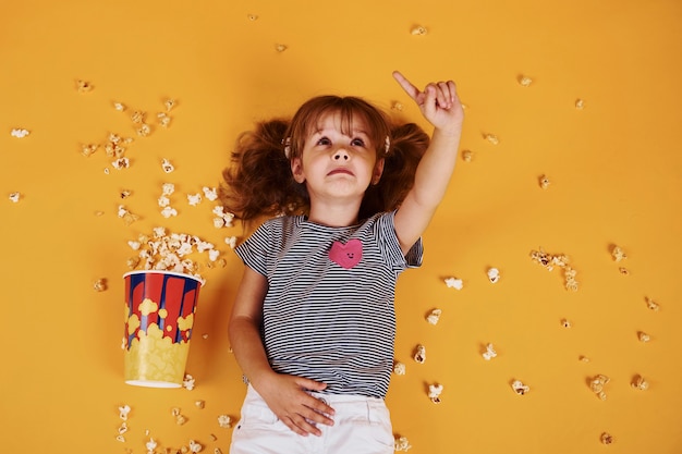 Cute little girl with popcorn lying down on the yellow floor.