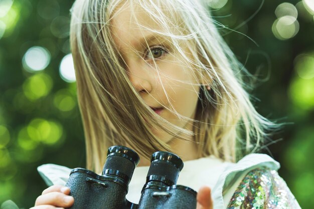 Bambina sveglia con un binocolo retrò in un parco cittadino