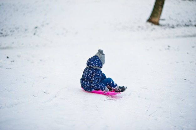 Милая маленькая девочка с санями блюдце на открытом воздухе на зимний день.